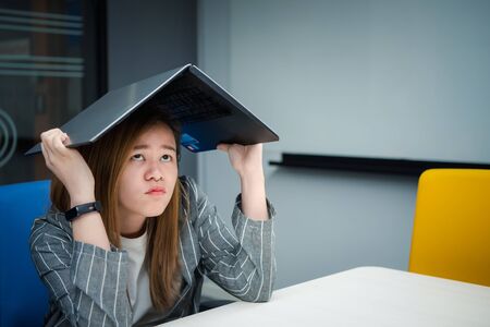Asian woman is student,businesswoman working by computer notebook, laptop in office meeting room with whiteboard background with annoyed, displeased emotion in concept working woman,unhappy in lifeの写真素材