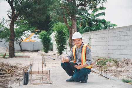 Asian man civil construction engineer worker or architect with helmet and safety vest working and holding a touchless tablet computer for see blueprints or plan at a building or construction siteの写真素材