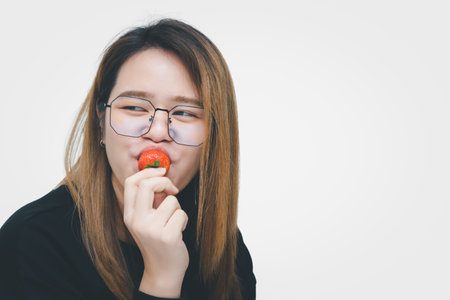 Asian pretty woman holding and eating fresh strawberry is red berry fruit color and sweet juicy with enjoy and happy emotion in concept food, healthy eating in lifeの写真素材