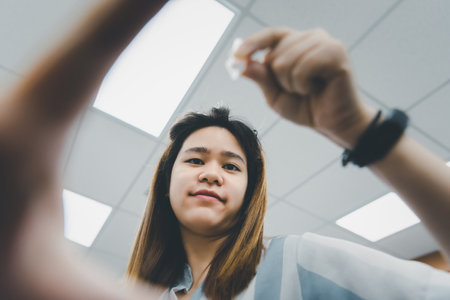 Asian woman use eye drop or artificial tears by drops in to the eye for someone else (POV) for inflammation or dryness problem therapy of eyeball for eyes healthの写真素材