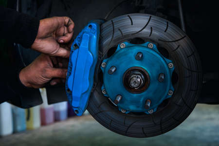 Car mechanic or serviceman disassembly and checking a disc brake and asbestos brake pads for fix and...