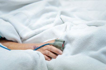 Patient asian elder woman 80s flu covid19 with pulse gauge for heartbeat measuring and blood pressure on a patient elderly finger on patient bed in intensive care unit (ICU.) room at hospitalの写真素材