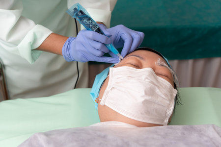 Asian woman eyebrow tattooing by doctor specialist in Eyebrow tattoo clinic or Eyebrow embroidery clinic for tattoo or correction use COVID-19 prevention policy protect by use mask and face shieldの写真素材