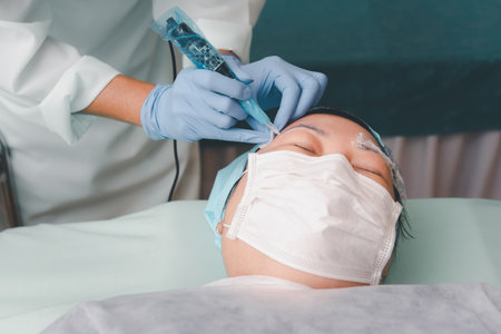 Asian woman eyebrow tattooing by doctor specialist in Eyebrow tattoo clinic or Eyebrow embroidery clinic for tattoo or correction use COVID-19 prevention policy protect by use mask and face shieldの写真素材