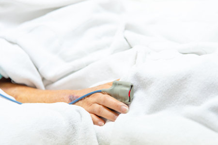 Patient asian elder woman 80s flu covid19 with pulse gauge for heartbeat measuring and blood pressure on a patient elderly finger on patient bed in intensive care unit (ICU.) room at hospitalの写真素材