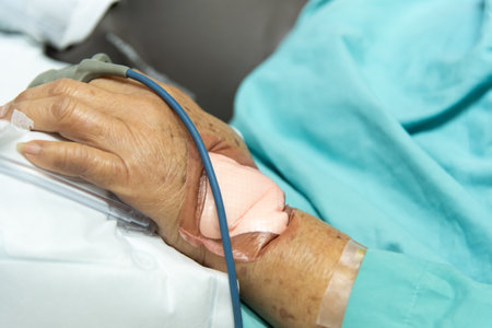 Patient asian elder woman 80s flu covid19 with pulse gauge for heartbeat measuring and blood pressure on a patient elderly finger on patient bed in intensive care unit (ICU.) room at hospitalの写真素材