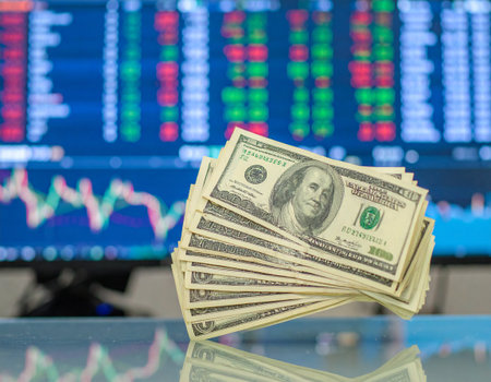 AI generated pile of crisp banknotes on reflective glass surface with active trading floor backdrop showing real-time stock market data and financial monitorsの素材