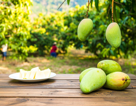 AI generated A rustic wooden table piled with fresh mangoes including halved fruits and sliced pieces on white plate Background shows mango orchard with farmers harvesting agriculture conceptsの素材