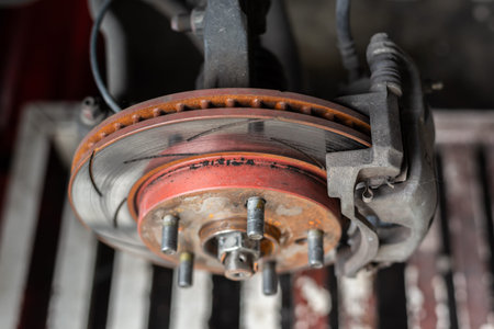 Closeup of car brake disc rotor and caliper showing wear rust and mechanical detail in garage environment highlighting maintenance safety and automotive repair concept