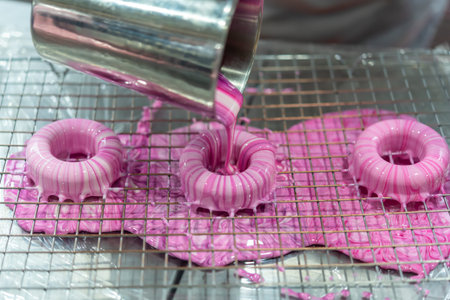 Fresh donuts being coated with pink glaze on wire rack showing baking process glossy texture and sweet dessert preparation in kitchen