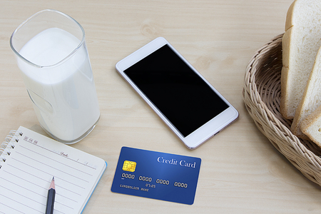 business work on wooden table milk with cut bread, credit card and mobile phoneの写真素材