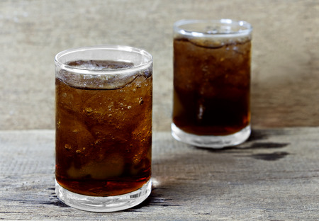 Glass of cola with ice on wooden table