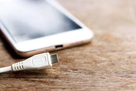 Charger cable for mobile phone on wooden table.