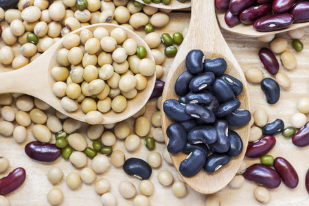 Many types of beans are separated in a spoon on a wood table such as mung bean, soybean, black bean,...