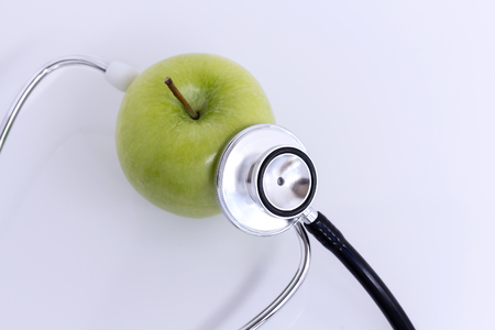 Stethoscope and green apple isolated on white table background. The stethoscope is a medical instrument for listening to the action of someone's heart or breathing. with copy space for your text.の写真素材