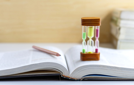 Sand dropping through the bulb of the hourglass and textbook placed on the table. with copy space for your text.の写真素材