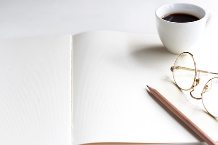Notebook, pencil, and cup of coffee on the white table. Space for your text or message.