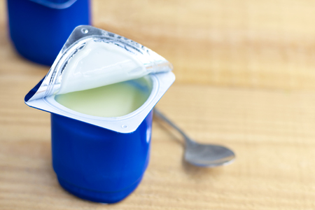 A breakfast of yogurt and a spoon placed on a wood table. Yogurt made from milk fermented by added bacteria, often sweetened and flavored.の写真素材
