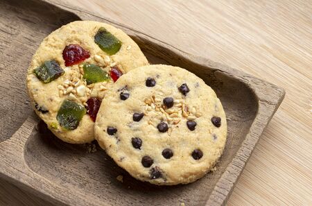Chocolate chip cookie and mixed fruits cookie with wooden tray on the wood table. Delicious homemade baked cookie.の写真素材