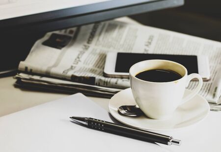 Cup of coffee with Newspaper, pen and smartphone on white table.の写真素材