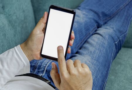 Men sit and relax on the couch and hold the mobile phone in hand.の写真素材