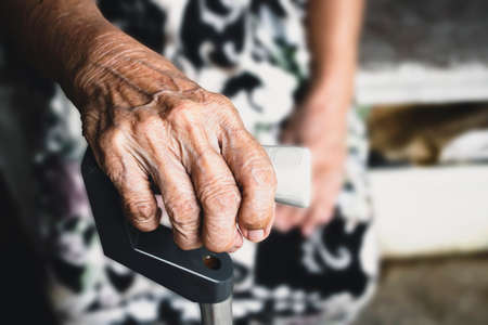 The hands of an elderly woman have curly fingers and wrinkled, holding the old cane sitting alone.の写真素材