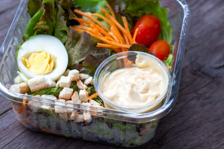 Salad made from fresh vegetables, carrots, tomatoes, chicken eggs, slices of bread and salad dressing packed in a box made of plastic.の写真素材
