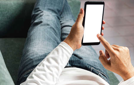 A man lying on the sofa resting and holding a smartphone in his hand.の写真素材