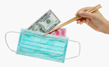 The hand of female holds the chopsticks, which clamp mask,  yuan and the dollar banknote. Doctor mask fitting over the nose and mouth to protect against dust or virus.の写真素材