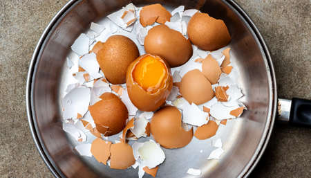 Broken eggshells and eggs in a pan on the cement floor.