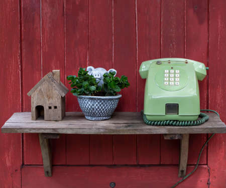 An antique telephone is placed on a shelf behind a red wooden plank.の写真素材