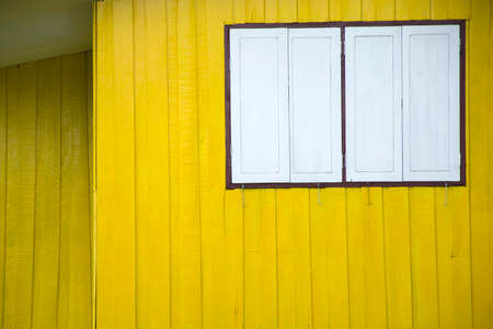 Yellow wood wall background, old wooden with yellow paint arranged vertically. It's the wall of an old wooden house. with a white window that is closed.の写真素材