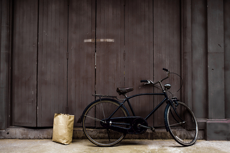 Old bicycle leaning against old wooden doors. With a brown paper bag resting on the back ground.の写真素材
