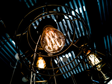 Tungsten orange light bulb hanging on the inside of the building with a black iron fence around,Lighting in buildings with multi-colored electric lamps,soft focus.high contrast format.の写真素材