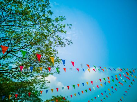 Colorful flags, colorful party decorations, small triangular flags to celebrate the party with the blue sky and clouds as the holiday concept background.の写真素材