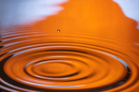 water drop splash in a glass orange-colored shot of water that is dripping and reflecting water.の写真素材