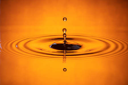 water drop splash in a glass orange-colored shot of water that is dripping and reflecting water.の写真素材