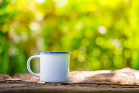White enamel coffee mug on a wooden table in the gardenの写真素材