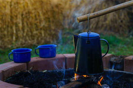A kettle and two cups of hot coffee on the background of a burning fireの写真素材