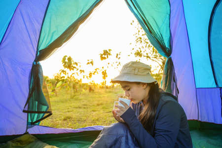 young girl in a tent and holding a cup  in the morning at sunrise in the forestの写真素材