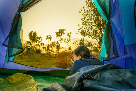 young girl in a tent and holding a camera in the morning at sunrise in the forest.soft focus.の写真素材