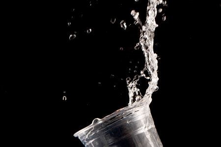 Drinking water splashing from the glass on black backgroundの写真素材