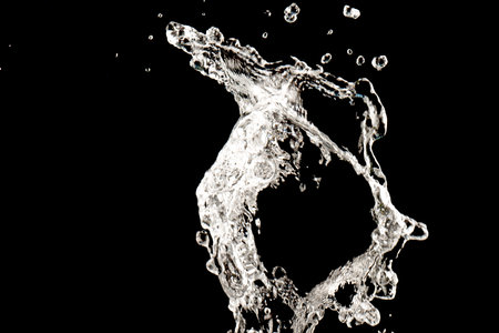 Drinking water splashing from the glass on black backgroundの写真素材