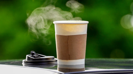 coffee takeaway in a paper cup on top of the car roof green tree background at sunrise in the morning,  selective focus, soft focus.の写真素材