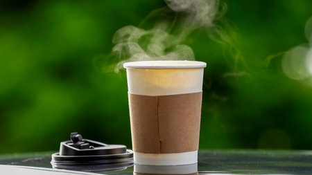 coffee takeaway in a paper cup on top of the car roof green tree background at sunrise in the morning,  selective focus, soft focus.の写真素材