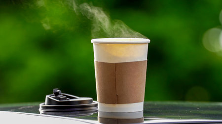 coffee takeaway in a paper cup on top of the car roof green tree background at sunrise in the morning,  selective focus, soft focus.の写真素材