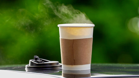coffee takeaway in a paper cup on top of the car roof green tree background at sunrise in the morning,  selective focus, soft focus.の写真素材