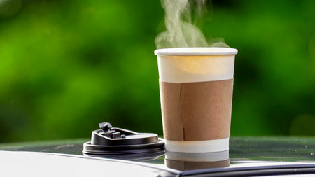 coffee takeaway in a paper cup on top of the car roof green tree background at sunrise in the morning,  selective focus, soft focus.の写真素材