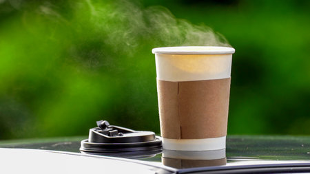 coffee takeaway in a paper cup on top of the car roof green tree background at sunrise in the morning,  selective focus, soft focus.の写真素材