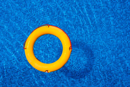 Top view of lifebuoy floating in blue swimming pool, soft focus.